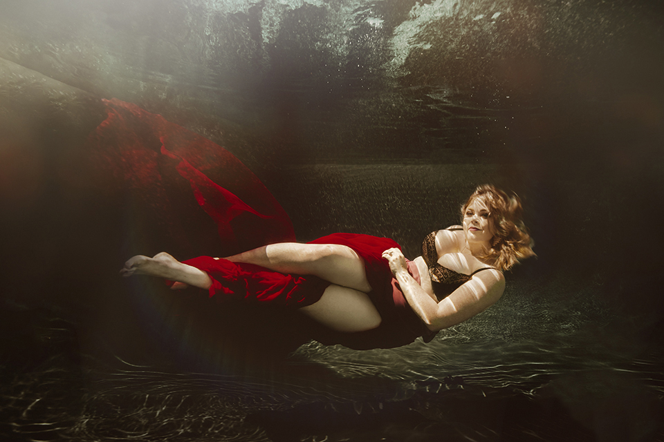 Women posing underwater in a red skirt and a black bra.